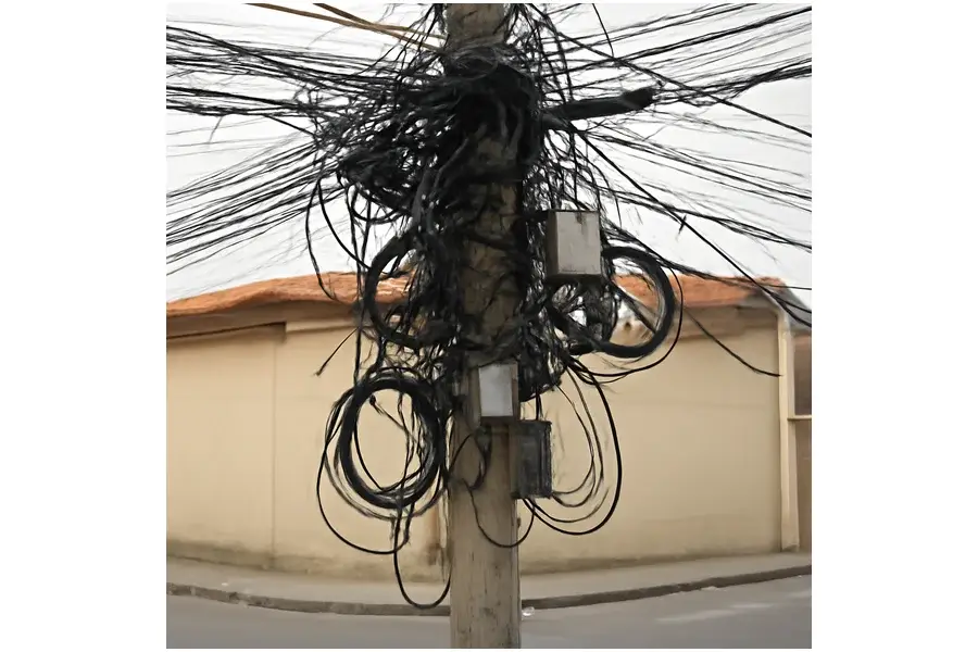 Poste urbano brasileiro com grande emaranhado de cabos variados pendurados e entrelaçados.