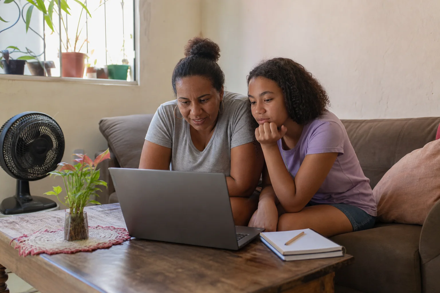 Mãe e filha usando um notebook na sala de casa.
