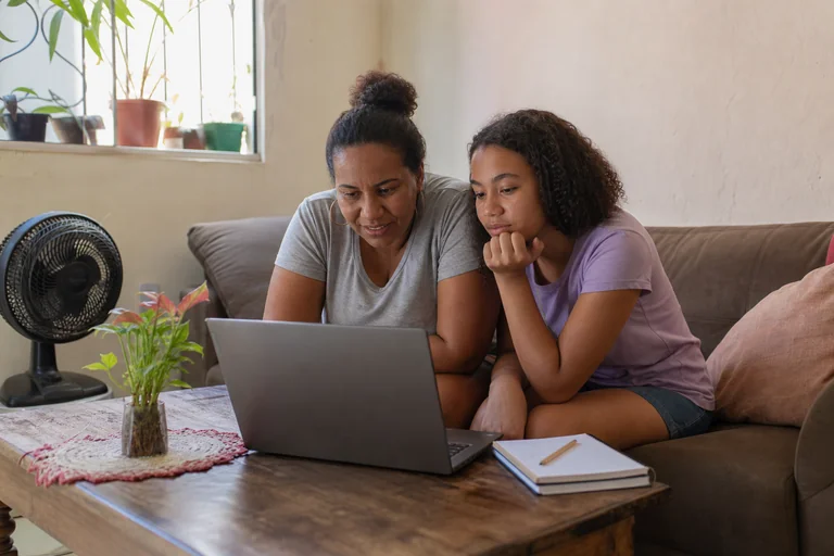 Mãe e filha usando um notebook na sala de casa.