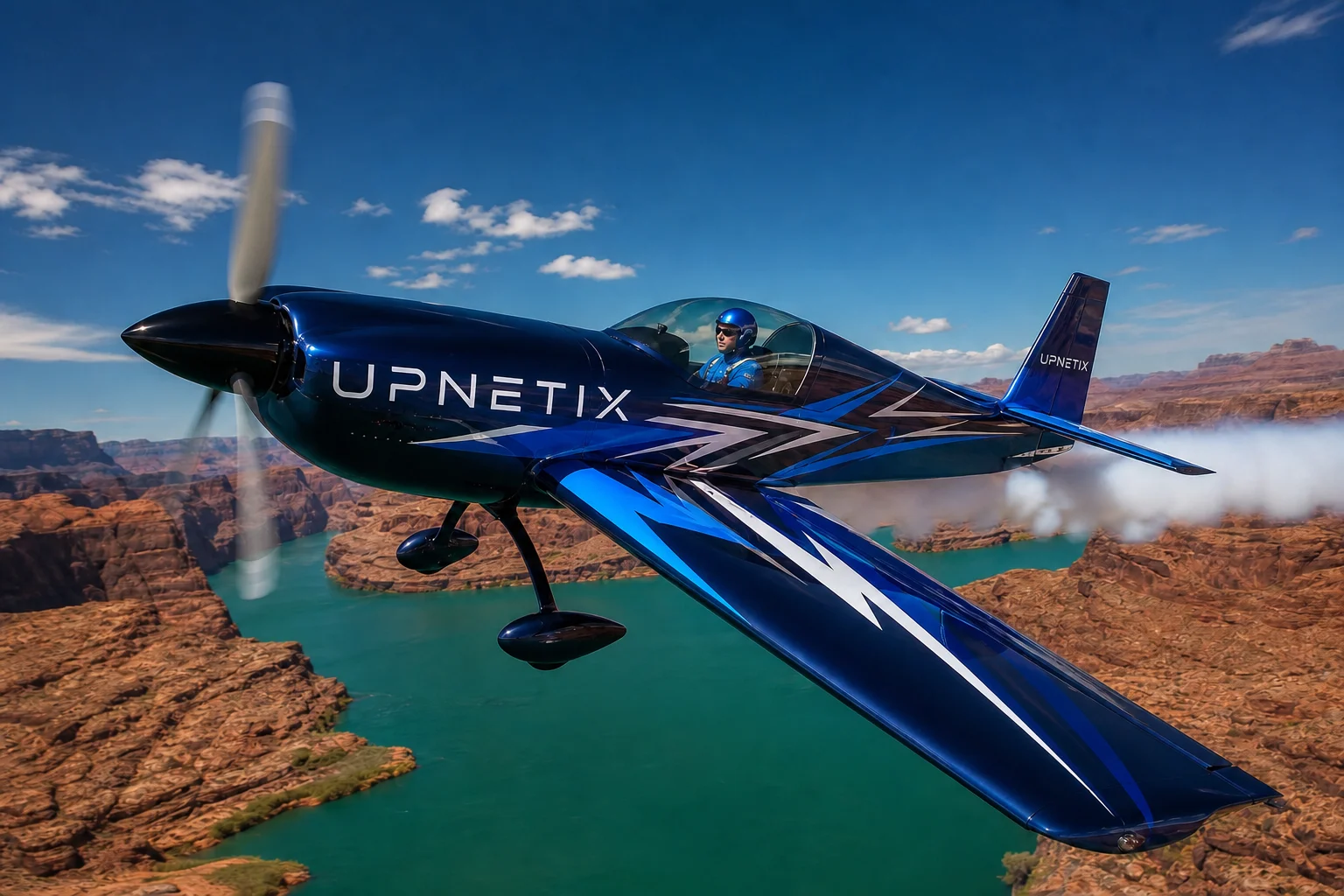Avião acrobático com a marca Upnetix em voo baixo sobre o mar entre cânions, piloto visível no cockpit.