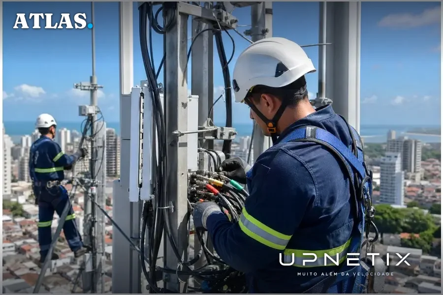 Técnicos realizando manutenção em torre de backbone de fibra óptica em área urbana brasileira.